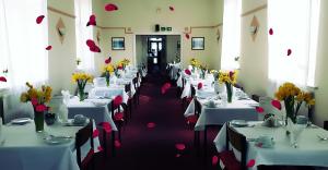 Elsinore Hotel Llandudno في خلنددنو: غرفة بها طاولات بيضاء عليها زهور