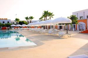 una piscina con sombrillas blancas, mesas y sillas en Chiusurelle Village Resort, en Punta Prosciutto