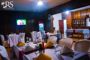 a dining room with tables and white chairs and a tv at Riverside Resort Hotel Kabale in Kabale