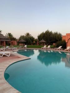 uma grande piscina azul com cadeiras e guarda-sóis em Villa avec piscine a Marrakech em Marrakech