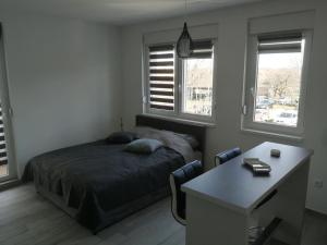 a bedroom with a bed and a desk and two windows at DANICA in Sremska Mitrovica