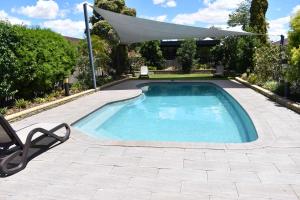 a swimming pool with a white umbrella and a chair at Best Western Plus All Settlers Motor Inn in Tamworth