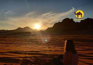 a woman sitting on the beach watching the sunset at Wadi Rum Dew in Wadi Rum