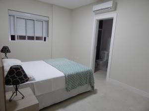 a white bedroom with a bed and a window at Apto. Novo e decorado. in Bombinhas