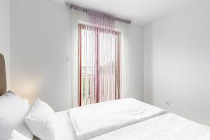 a white bedroom with a bed and a window at Apartments Mike in Malinska