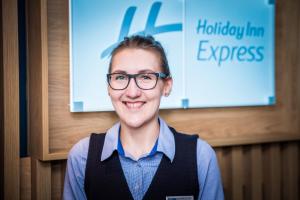 Holiday Inn Express - Exeter - City Centre, an IHG Hotel في إكسيتير: امرأة ترتدي نظارات تقف أمام علامة