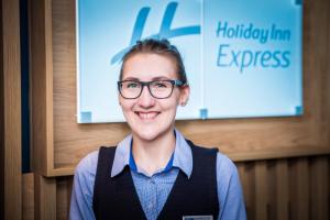 a woman wearing glasses standing in front of a sign at Holiday Inn Express - Exeter - City Centre, an IHG Hotel in Exeter