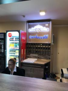 una mujer sentada en un mostrador delante de una máquina de refrescos en Royal Hotel en Cserkeszőlő