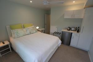 a bedroom with a white bed and a small kitchen at Hahei Pavillion Guest House in Hahei
