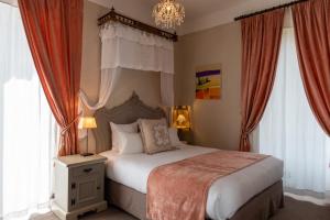 a bedroom with a bed with a chandelier and windows at Domaine de Beaupré - Hotel The Originals Relais in Guebwiller