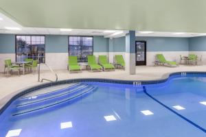 Holiday Inn Express Hotel & Suites Providence-Woonsocket, an IHG Hotel في Woonsocket: مسبح وكراسي خضراء وطاولات في مبنى