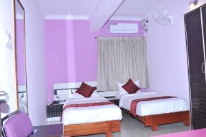 a bedroom with two beds and a window with purple walls at Brahma Inn in Bangalore