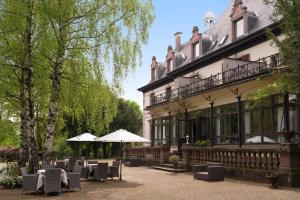 um pátio com mesas e guarda-sóis em frente a um edifício em Domaine de Beaupré - Hotel The Originals Relais em Guebwiller