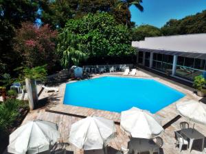 a large blue swimming pool with umbrellas and chairs at Sayuri hotel in Foz do Iguaçu