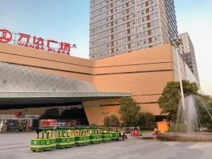 a green train in front of a building with a fountain at 7Days Inn Hangzhou Wanda Square in Hangzhou