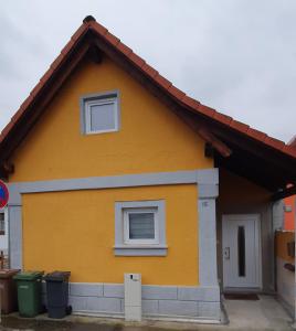 a yellow house with two windows and two trash cans at Ferienwohnung Häusla in Hirschaid