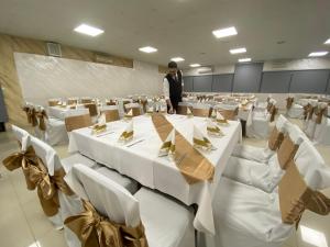 un homme debout dans une pièce avec des tables et des chaises blanches dans l'établissement Hotel Moment, à Velika Plana