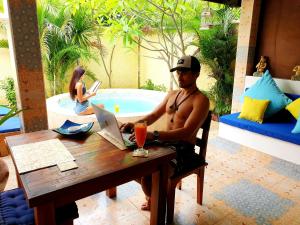 a man sitting at a table with a laptop at Cinta Cottages in Gili Trawangan