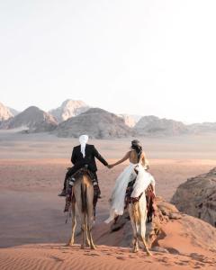 une mariée et un marié se déplaçant à dos de chameau dans le désert dans l'établissement WADI RUM STAR WARS CAMP, à Wadi Rum