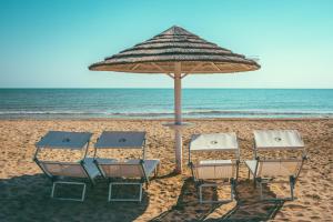 トルトレート・リドにあるResidence Palazzo Gasparroniのビーチでの椅子2脚とパラソル1本