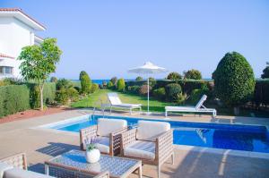 a swimming pool with chairs and a table next to a house at Atlantis Gardens in Mazotos