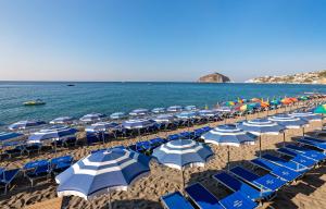 a beach with blue and white umbrellas and the ocean at Hotel San Giorgio Terme in Ischia