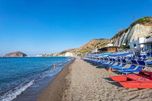 a beach with blue and red chairs and the ocean at Hotel San Giorgio Terme in Ischia