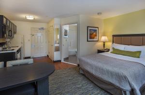 Candlewood Suites Louisville Airport, an IHG Hotel في لويزفيل: غرفة نوم بسرير وطاولة ومطبخ