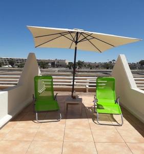 due sedie verdi e un ombrellone su un balcone di Studio Naturiste "SUNSHINE" Héliopolis FG 14 a Cap d'Agde