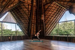 a woman doing a yoga pose in a room with windows at The Beach Tulum Hotel in Tulum