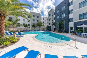 a pool with blue chairs and palm trees in front of a building at Staybridge Suites - Naples - Marco Island by IHG in Naples