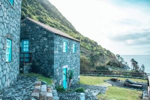 uma casa de pedra no lado de uma colina ao lado do oceano em Abrigo da Cascata - Casas de Campo - São Jorge em Calheta