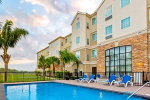 a swimming pool with blue chairs and a building at Staybridge Suites - Brownsville by IHG in Brownsville