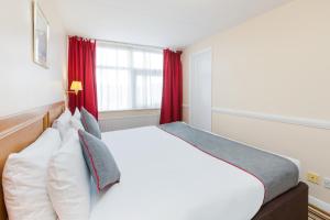 a bedroom with a large white bed with red curtains at OYO Stade Court Hotel in Hythe