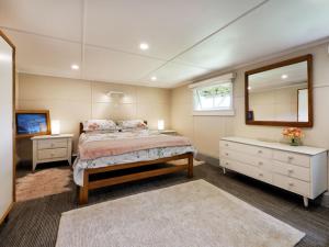 Un dormitorio con una cama, una cómoda y un espejo. en Surfer's Sunshine Cottage - Piha Holiday Home, en Piha