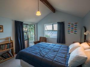 a bedroom with a blue bed and a window at Matai Cottage - Pakawau Bach in Pakawau
