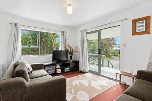 a living room with a couch and a tv at The Taranui Cottage - Mangawhai Heads Holiday Home in Mangawhai