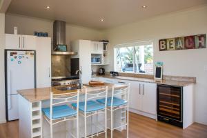 una cocina con armarios blancos y una barra con taburetes en Waterfront Wonder - Matarangi Holiday Home, en Matarangi