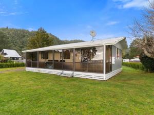 a white house on a lawn with a clock on top at Relax Lakeside - Lake Rotoiti Bach in Rotoiti +10 photos