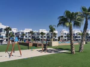 un parque con un parque infantil con palmeras y apartamentos en condominio en Oasis Beach juan en Guardamar del Segura