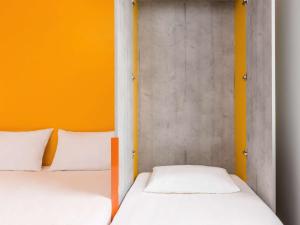 Duas camas num quarto com uma parede laranja em ibis budget Rouen Nord Isneauville em Isneauville