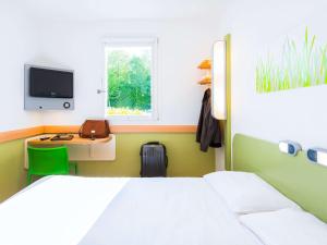 a bedroom with a bed and a desk with a tv at ibis budget Rennes Route de Saint Malo in Montgermont