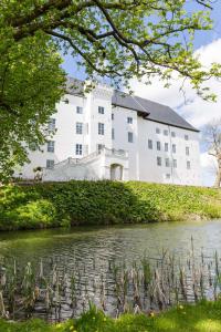 ein großes weißes Gebäude auf einem Hügel neben einem Fluss in der Unterkunft Dragsholm Slot in Hørve