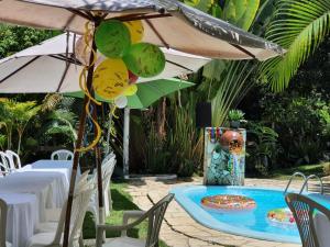 a table with an umbrella and some chairs and a pool at CHÁCARA RECANTO DA MATA in Satuba