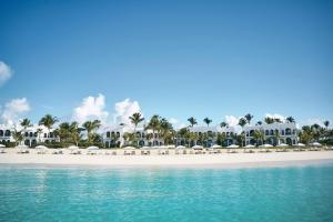 einen Strand mit weißen Sonnenschirmen und Stühlen darauf in der Unterkunft Cap Juluca, A Belmond Hotel, Anguilla in West End Village