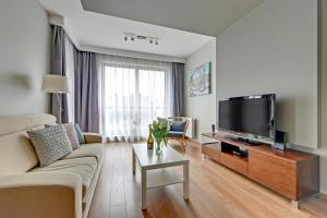 Apartments RIVA - Nadmorski Dwór Premium في غدانسك: غرفة معيشة مع أريكة وتلفزيون بشاشة مسطحة