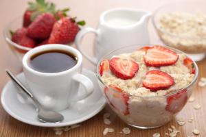 un tazón de avena con fresas y una taza de café en Волшебный Край на Менделеева, en Ufa