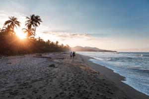 duas pessoas caminhando na praia ao pôr do sol em Bohemia Beach Tayrona em Guachaca