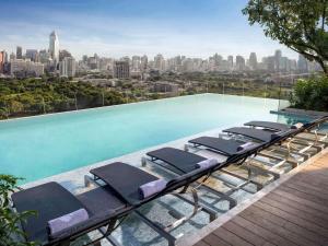 a row of chaise lounge chairs on a pool with a city skyline at SO/ Bangkok in Bangkok