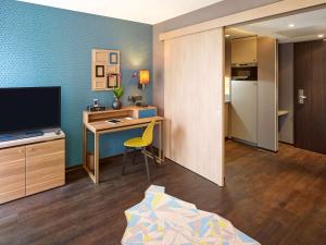 a small room with a desk and a tv and a bedroom at Aparthotel Adagio Köln City in Cologne